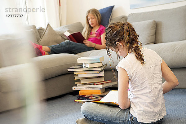 Two girls sitting in the living room reading books