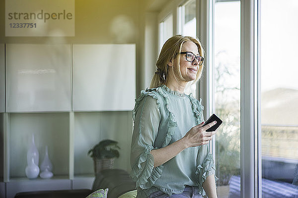 Portrait of content woman with smartphone looking out of window