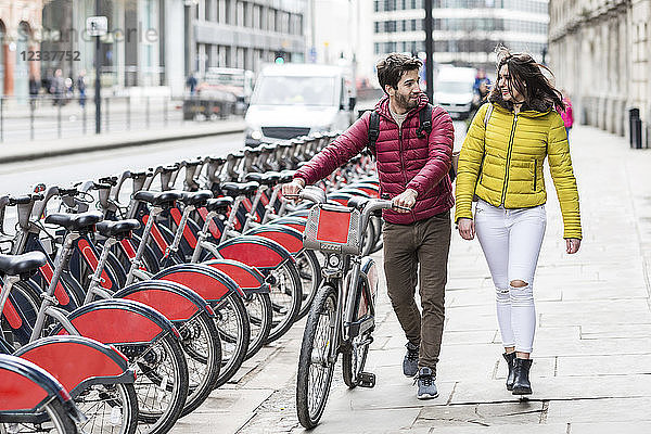 UK  London  young couple with bicycle from bike share stand walking in city