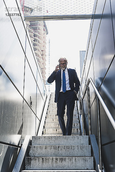 Smiling mature businessman on staircase in the city on cell phone