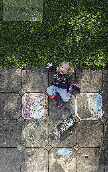 Smiling little girl drawing with chalk outdoors  top view