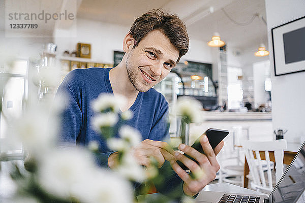 Portrait of smiling man in a cafe with cell phone and laptop