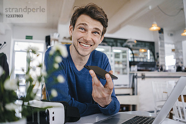 Smiling man in a cafe with cell phone and laptop