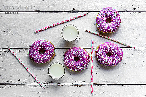 Four pink doughnuts  two glasses of milk and straws on white wood