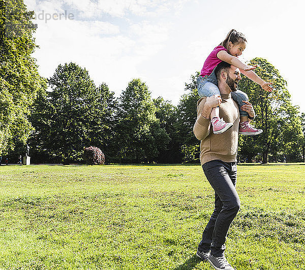 Happy father carrying daughter on shoulders in a park