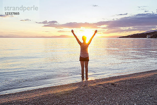 Greece  Pelion  Pagasetic Gulf  woman on the beach with raised arms at sunset  Kalamos in the background