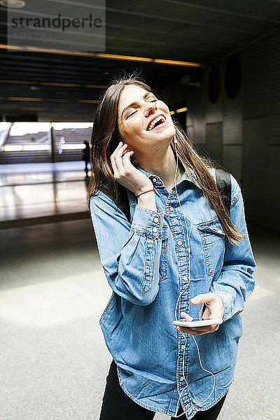 Portrait of happy young woman listening music with cell phone and earphones