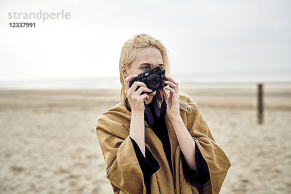 Netherlands  blond young woman taking photo with camera on the beach