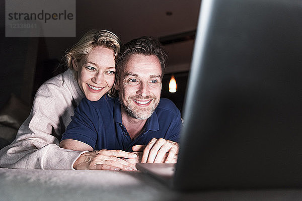 Happy couple lying on couch at home looking at laptop