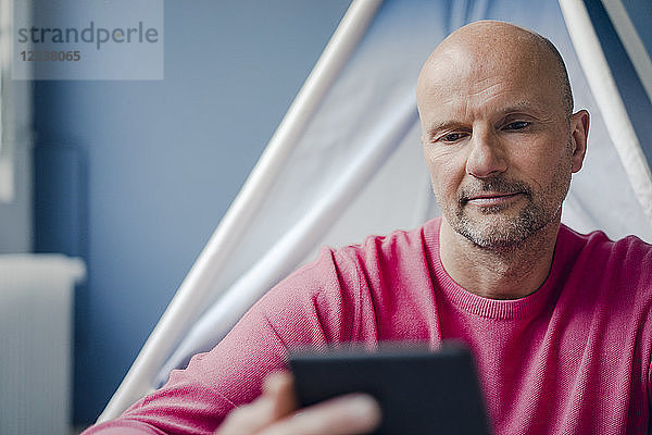 Mature man sitting at teepee indoors looking at cell phone
