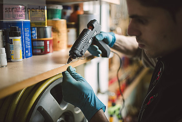 Man using a hot glue gun on shelf in workshop