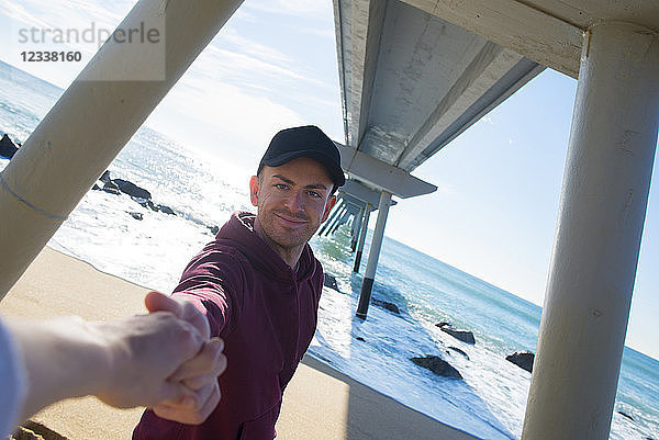 Man holding hand of woman under a bridge on the beach