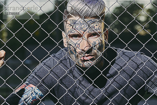Portrait of tattooed young man behind fence