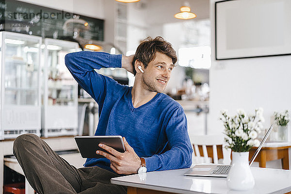 Smiling man in a cafe with earphone  laptop and tablet