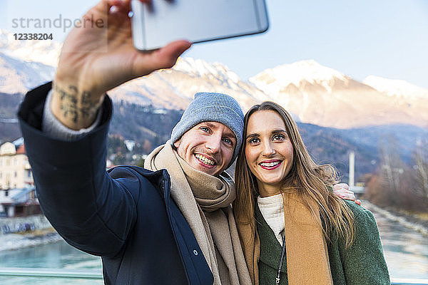 Austria  Innsbruck  portrait of happy young couple taking selfie with smartphone in winter