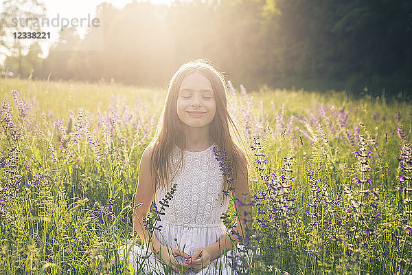 Portrait of smiling girl crouching on flower meadow at evening twilight