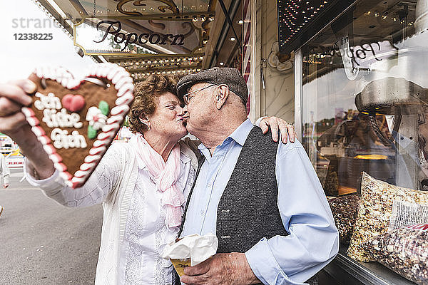 Senior couple with gingerbread heart kissing on fair