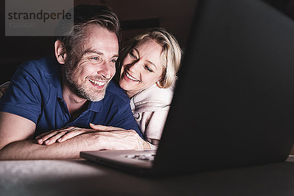 Happy couple lying on couch at home using laptop