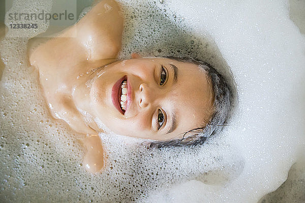 Portrait of happy little girl bathing in a tub