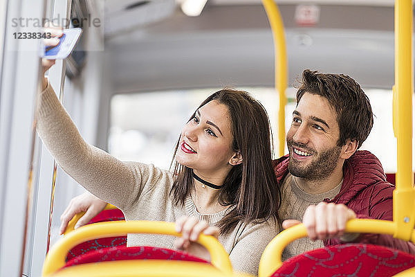 UK  London  portrait of smiling young couple taking selfie with smartphone in bus