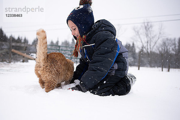 Junge spielt mit Katze im Schnee