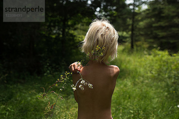 Blondhaariger Junge im Wald mit einer Wildblume auf der Schulter  Rückansicht