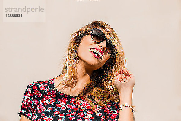 Blonde  elegante Frau mittleren Alters mit Sonnenbrille vor der Wand lachend