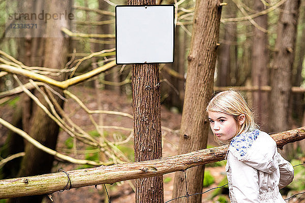 Mädchen blickt zurück im Wald neben einer leeren Anschlagtafel am Baumstamm