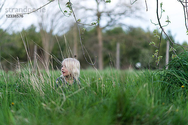 Blondhaariger Junge im langen Gras  der über die Schulter schaut