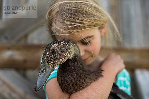 Mädchen mit geschlossenen Augen umarmt Bauernhof-Ente