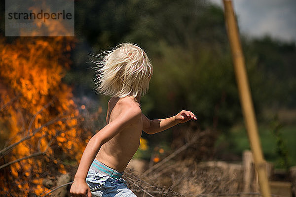 Blondhaariger Junge rennt vom Gartenfeuer weg