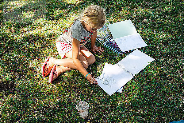 Mädchen sitzt auf Rasen und macht Hausaufgaben