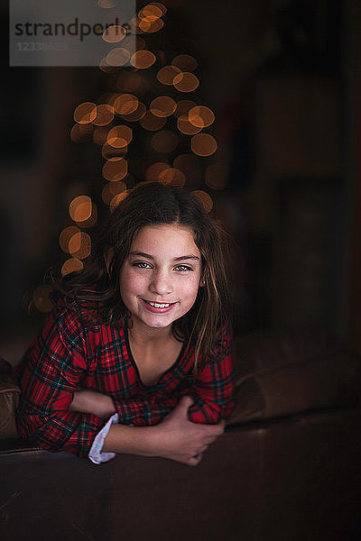 Mädchen lehnt über Sofa  lächelnd  Weihnachtsbaum im Hintergrund