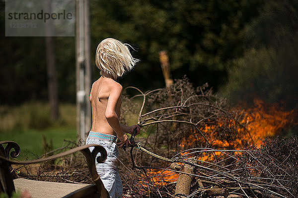 Blondhaariger Junge legt Baumzweig auf Gartenfeuer