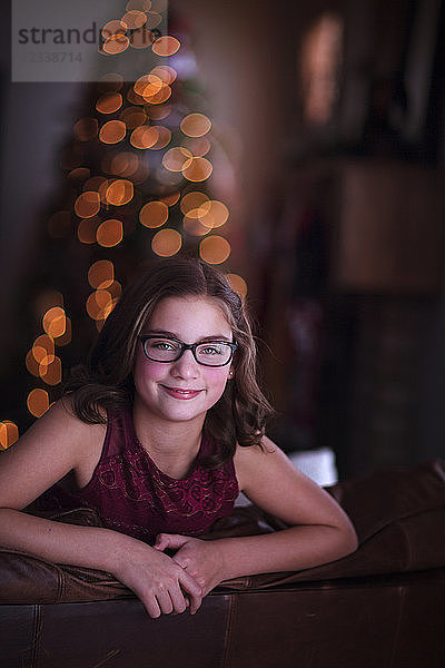 Mädchen lehnt über Sofa  lächelnd  Weihnachtsbaum im Hintergrund