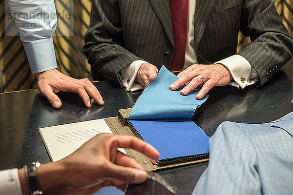 Schneider und Kunden betrachten Muster in einer traditionellen Schneiderei  Detail der Hände