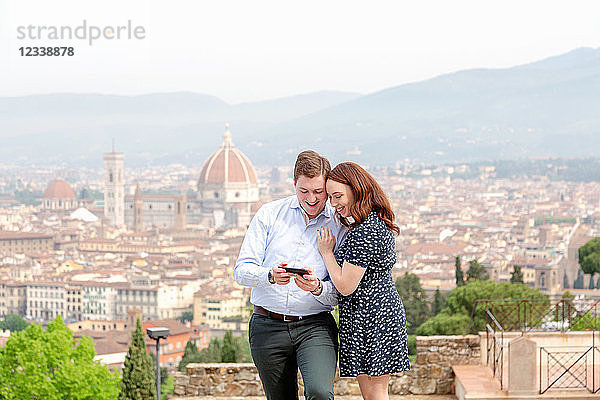 Junges Paar lächelt am Handy  Santa Maria del Fiore im Hintergrund  Florenz  Toskana  Italien