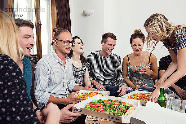 Eine Gruppe von Freunden unterhält sich bei Getränken und Pizza zu Hause