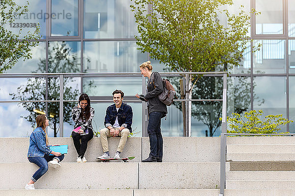 Vier junge erwachsene Studenten sitzen vor dem College auf einer Treppe und unterhalten sich