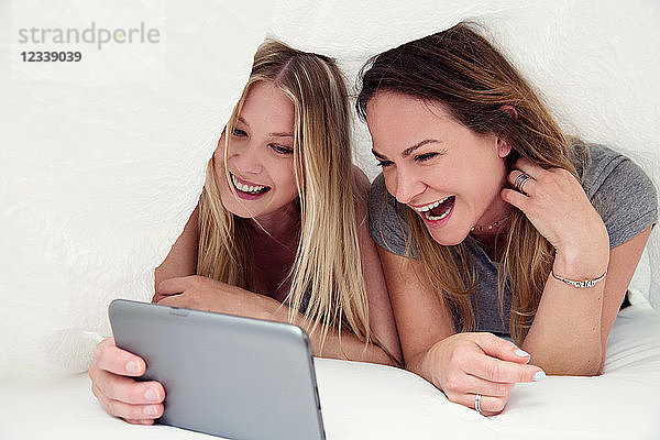Freunde unter dem Bettlaken mit digitalem Tablet lächeln