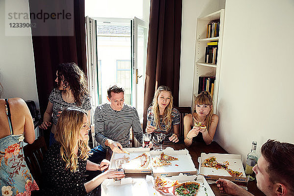 Eine Gruppe von Freunden unterhält sich bei Getränken und Pizza zu Hause