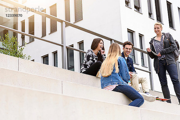 Vier junge erwachsene Studenten sitzen plaudernd auf einer Treppe vor dem College  Blick aus niedrigem Winkel