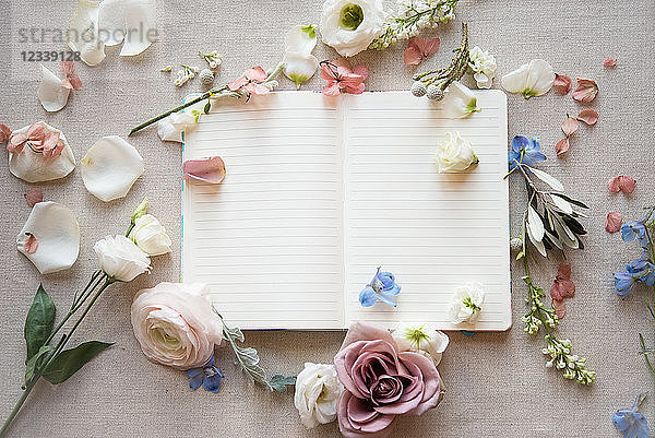 Stilleben eines leeren offenen Notizbuches mit pastellfarbenen Blütenköpfen  Blütenblättern und Stielen  Draufsicht