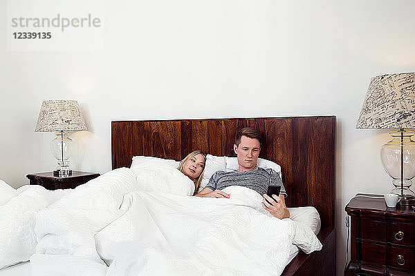 Im Bett liegendes Paar mit Mobiltelefon