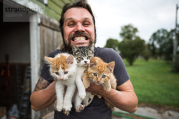 Mann grinst mit drei Kätzchen im Arm