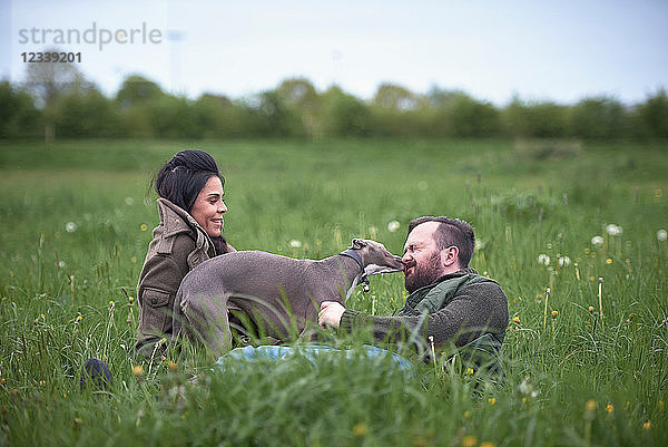 Liegender Mann und liegende Frau beim Feldspiel mit Hund