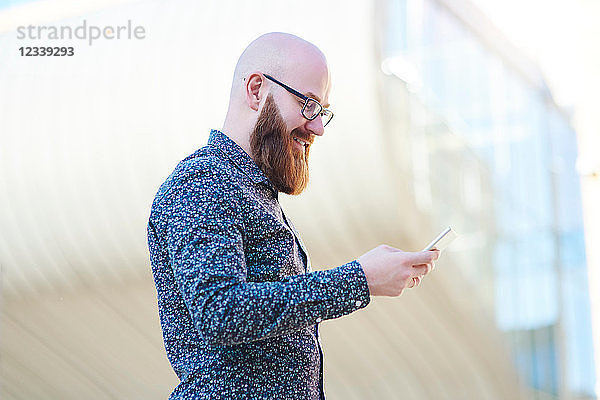 Bärtiger Mann schreibt auf Smartphone und lächelt