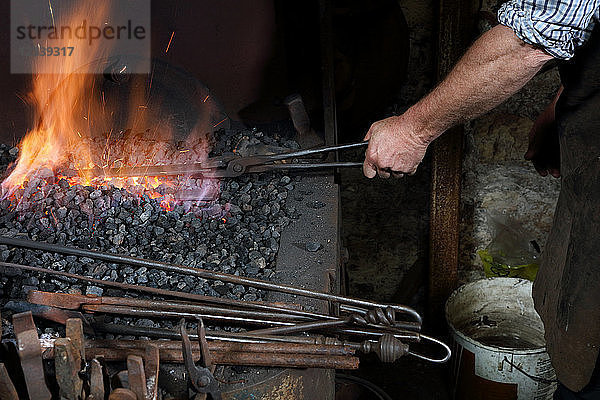 Schmied erhitzt Metall im Schmiedefeuer in der Schmiedewerkstatt  abgeschnitten