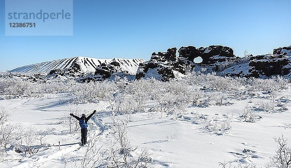 Mann auf Wanderweg im Schnee bei Sonnenschein  verschneite Landschaft  Lavafeld mit schneebedecktem Felsbogen  Vulkanlandschaft Krafla  Dimmuborgir Nationalpark  Mývatn  Island  Europa