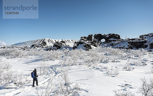 Mann auf Wanderweg im Schnee bei Sonnenschein  verschneite Landschaft  Lavafeld mit schneebedecktem Felsbogen  Vulkanlandschaft Krafla  Dimmuborgir Nationalpark  Mývatn  Island  Europa